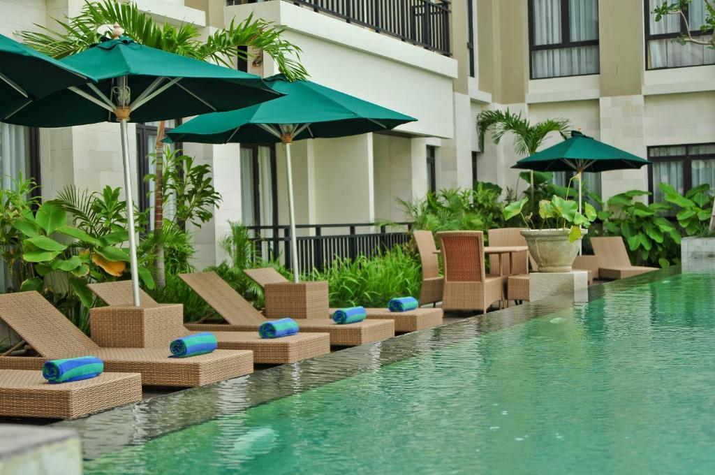 a pool with chairs and umbrellas next to a building at Grand Kuta Hotel and Residence in Legian