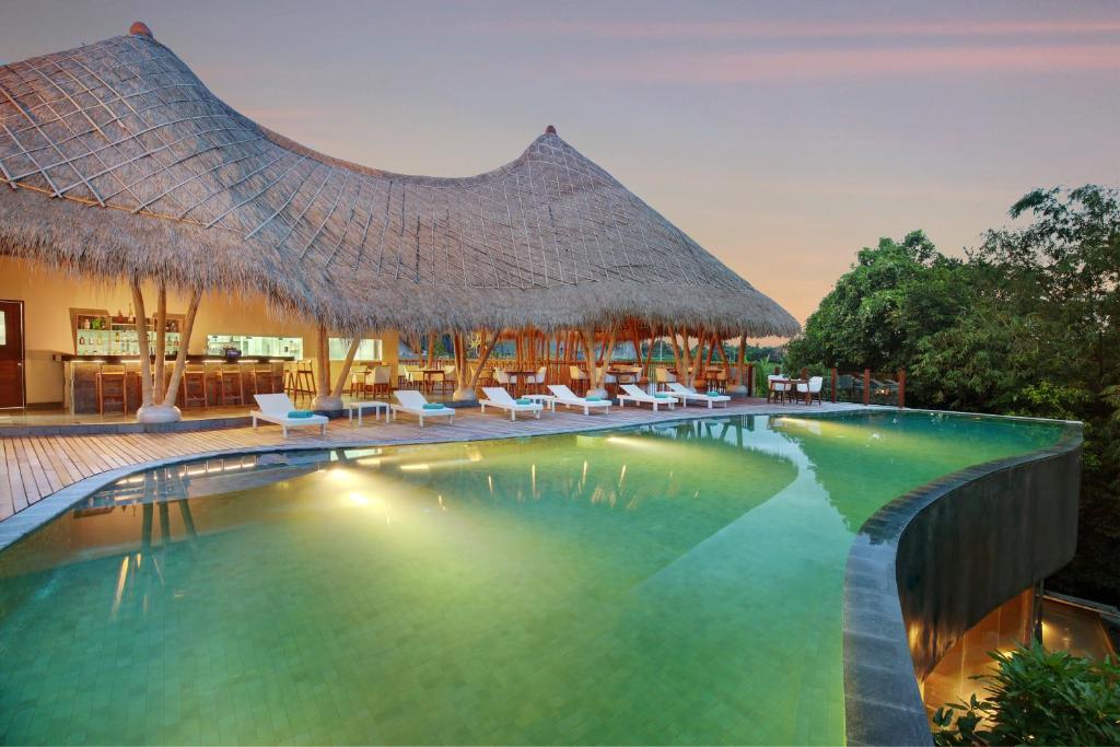 a resort swimming pool with chairs and a thatched roof at Theanna Villa and Spa Canggu in Canggu