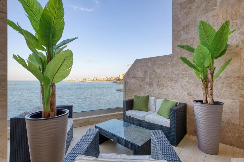 a patio with two plants and a couch and a table at 2BR Seafront Elegance with Balcony & Sea Views by 360 Estates in St. Paul's Bay