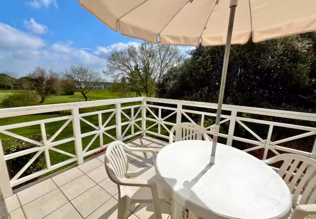 a white table and chairs on a balcony with an umbrella at Au calme, appartement au cœur du Golf - Piscine in Talmont