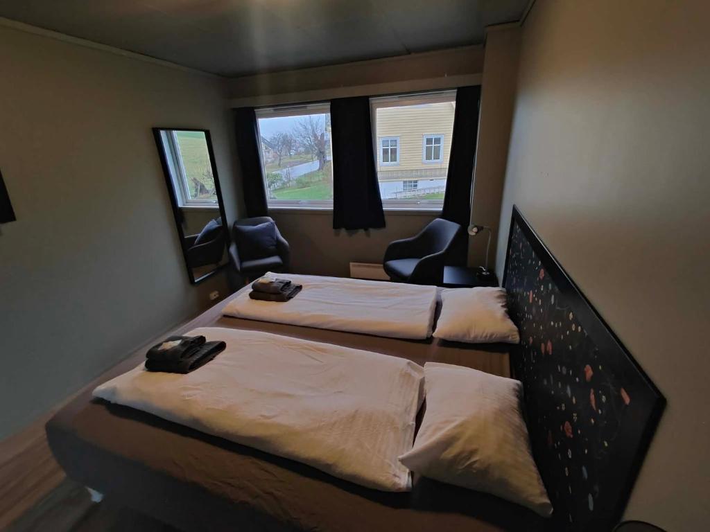 two beds in a room with two chairs and two windows at Gjøa Motell in Rosendal