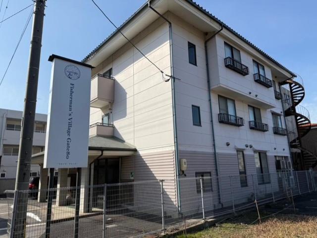 a white building with a sign in front of it at GATE80米子 無人宿 完全セルフ 予約メッセージ欄確認要す スマートロック 暗証番号チェックイン 素泊まり専門 アメニティ持参で格安滞在 セコム24h監視 駐車場7台 in Yonago