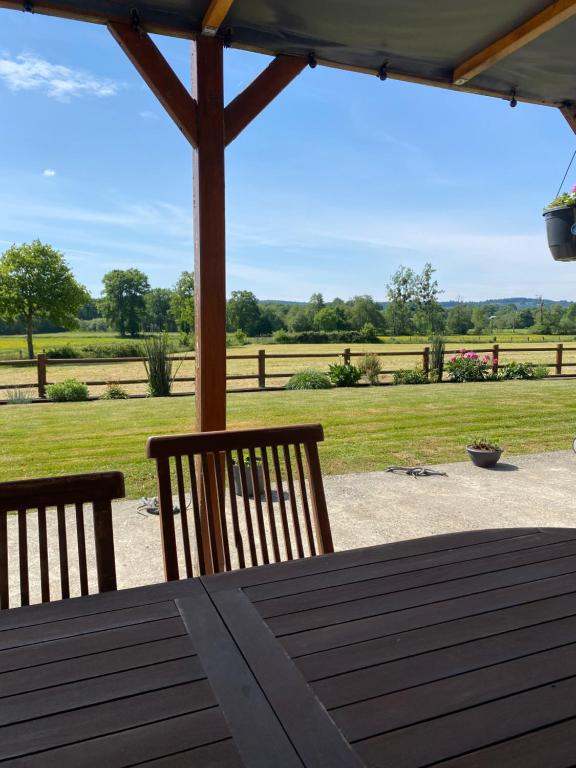 a wooden table with two chairs and a view of a field at Chambres d'hôtes de l'Eau dit Sée in Cuves