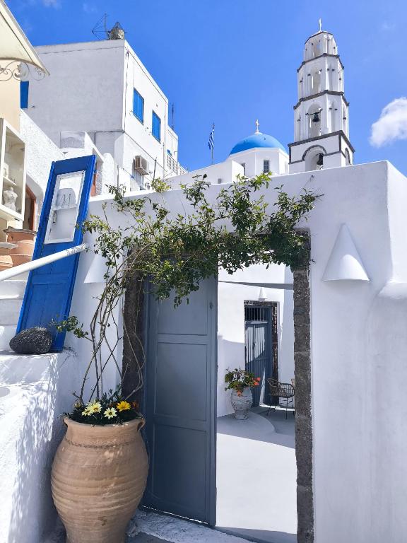 a white building with a blue door and a tower at Imarkellis Santorini Cave House with yard in Pyrgos