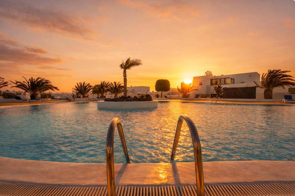 a resort swimming pool with a sunset in the background at Finca Thiago in Puerto Calero