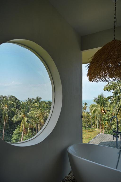 a bathroom with a round window with a tub and palm trees at Ocean Villa in Ko Phangan