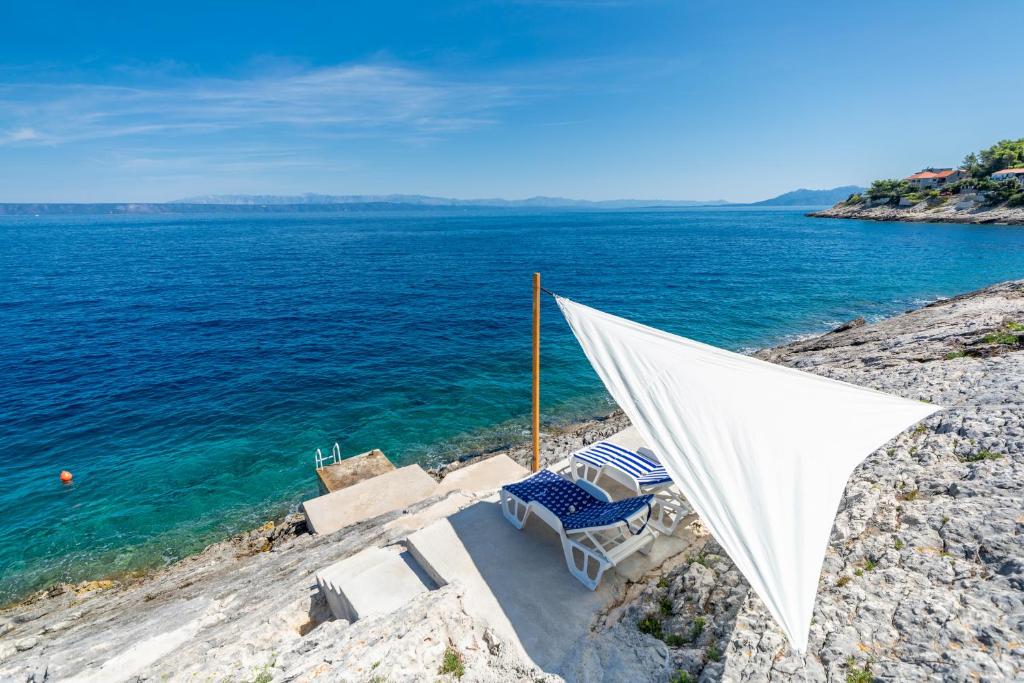 a hammock and two chairs on a rocky beach at Seafront Holiday Home - Private Jacuzzi in Blato
