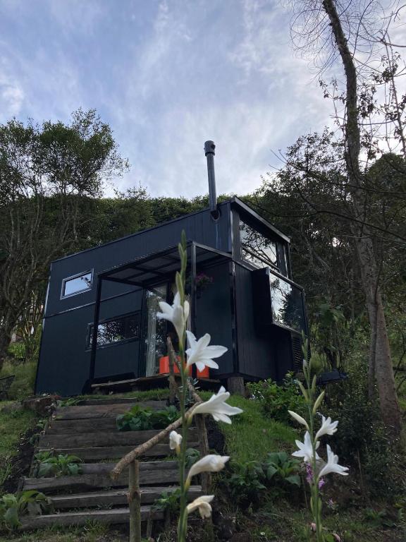 a black tiny house in the woods with flowers at La Tiny TINY HAUS in Bogotá