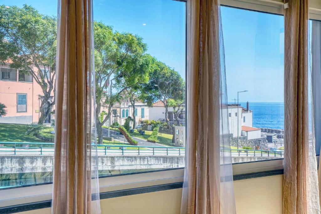 a window with curtains looking out at the ocean at Vilamar- Madeira Inn Group in Calheta