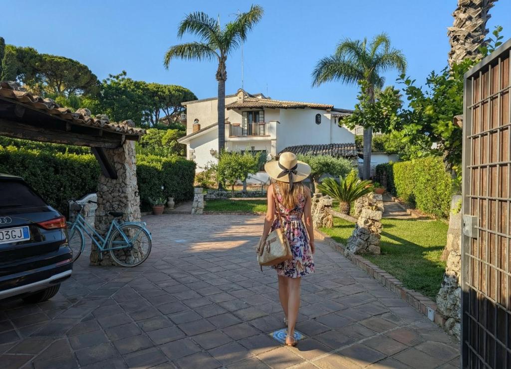 a woman in a dress and hat walking down a driveway at Azure Bay Chic Villa in Fontane Bianche