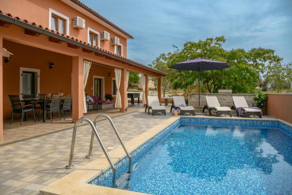 a pool with chairs and an umbrella next to a house at Villa Percan - Spacious Family Home with Private Pool on a 4000 Square Meter Plot in Krnica