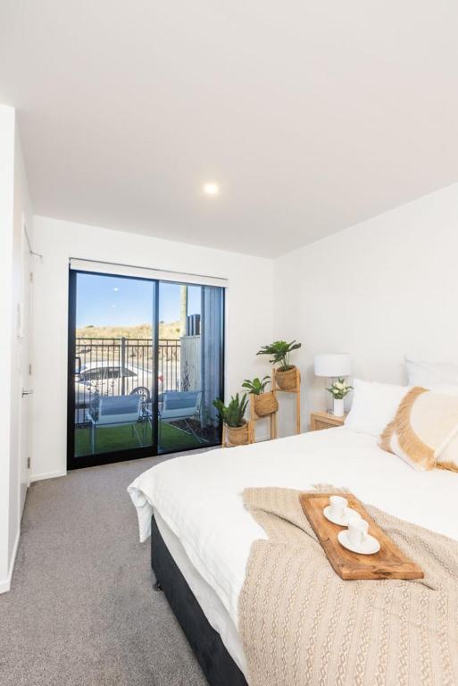 a white bedroom with a large bed and a balcony at Private ensuite room on the beach in Christchurch