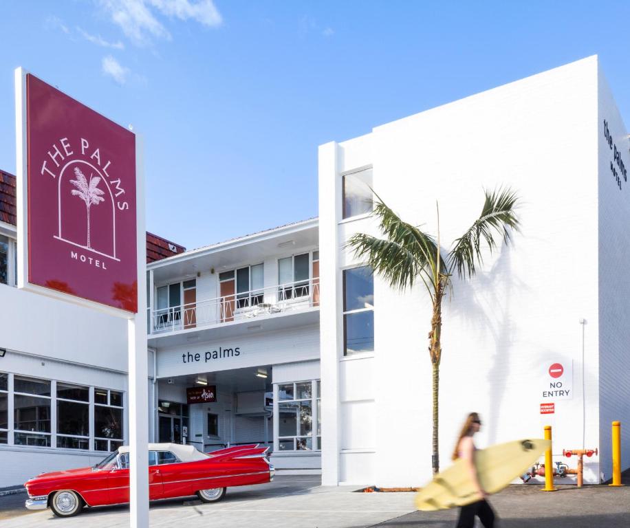 a red car parked in front of a building with a palm tree at The Palms Motel- Formerly Flinders Motel in Wollongong