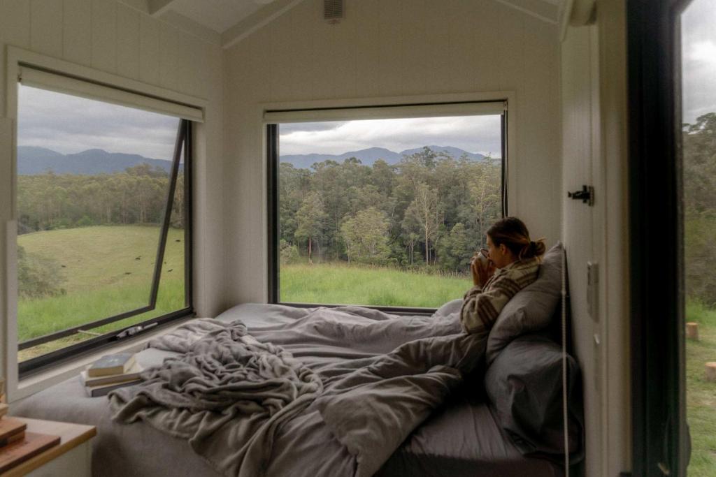 a woman sitting on a bed in a room with a window at Tiny Nancy in Bellingen