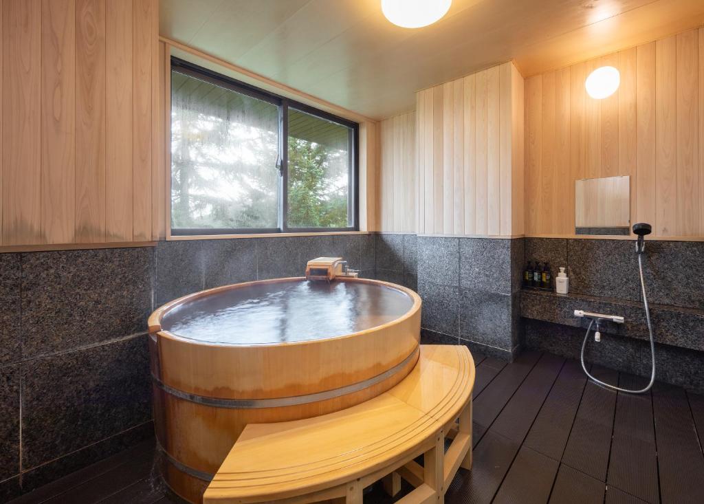 une grande baignoire en bois dans une salle de bain avec une fenêtre dans l'établissement Hotel Kanronomori, à Niseko