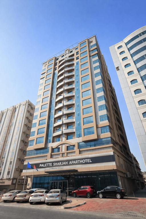 a large building with cars parked in front of it at Palette Sharjah Aparthotel formerly Royal Tulip in Sharjah