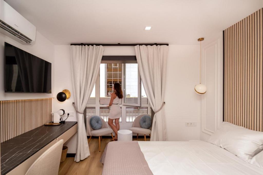 a woman standing in a bedroom looking out the window at Boutique Centro Hostal in Alicante