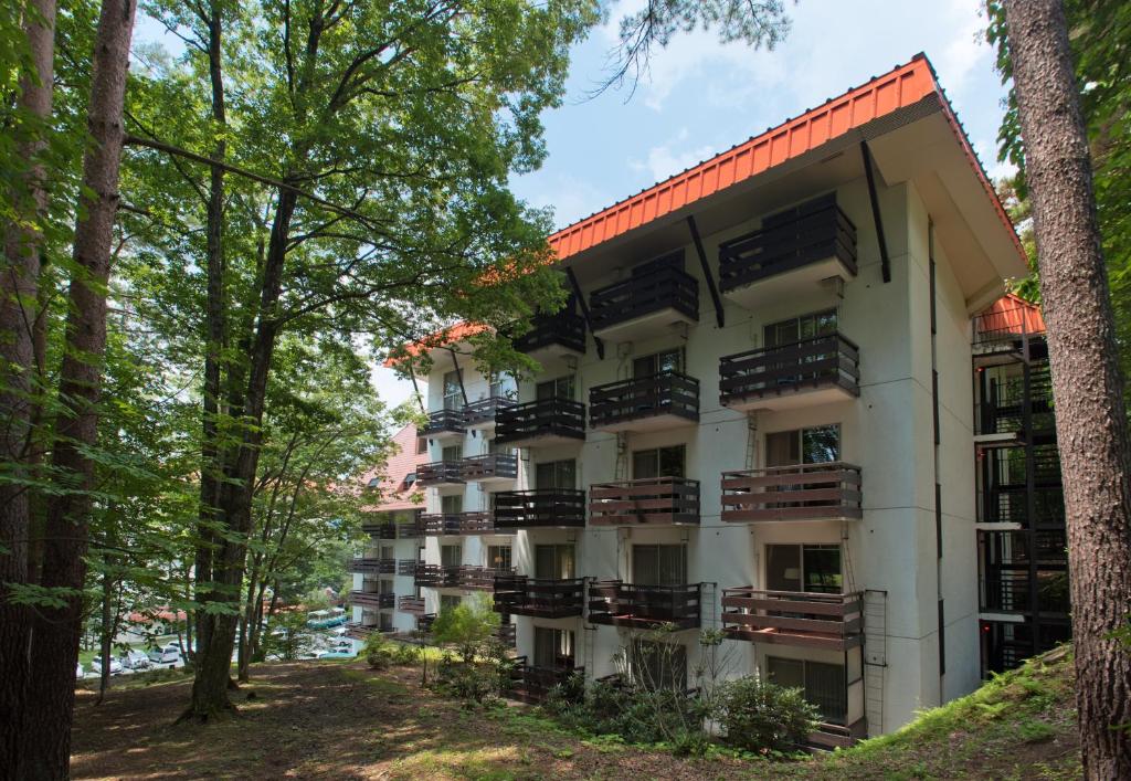 an apartment building with balconies and trees at Kusatsu Onsen Hotel Village in Kusatsu