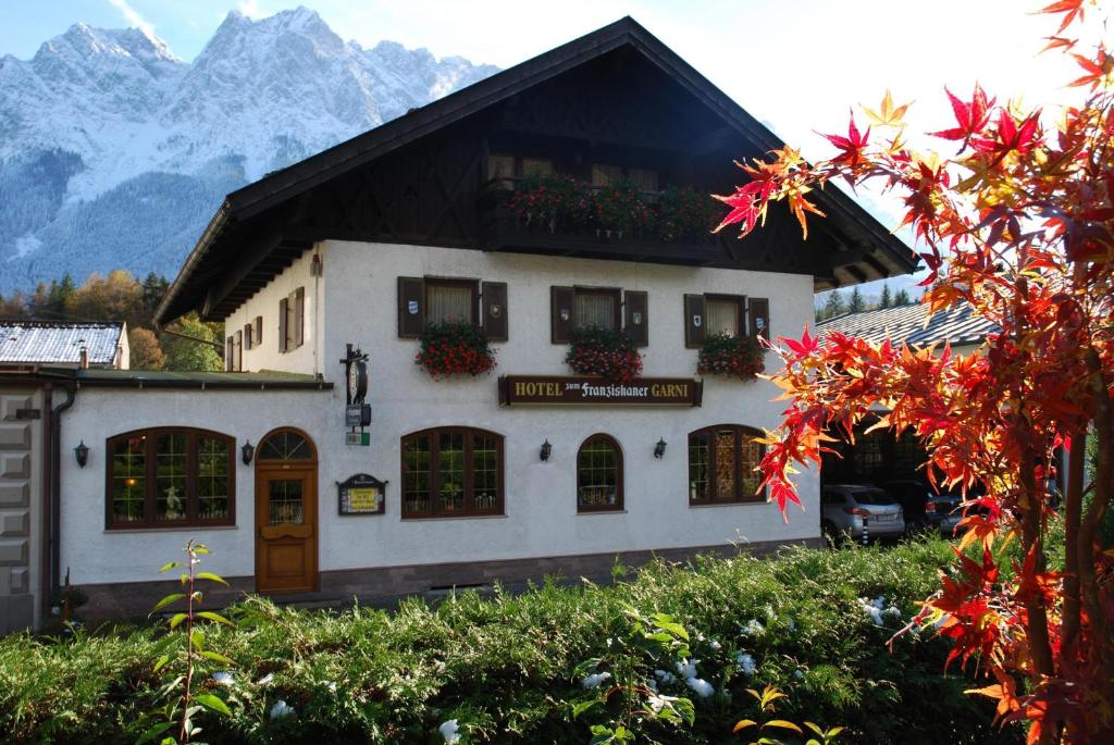 a white building with flowers on the windows and mountains at Zum Franziskaner in Grainau