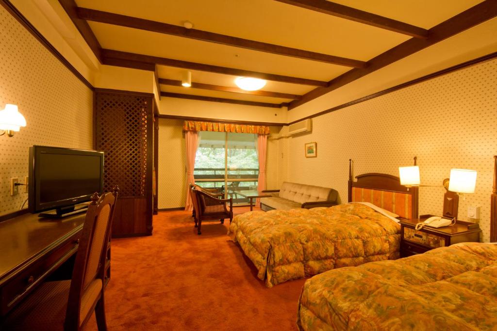 a hotel room with two beds and a flat screen tv at Kusatsu Onsen Hotel Village in Kusatsu