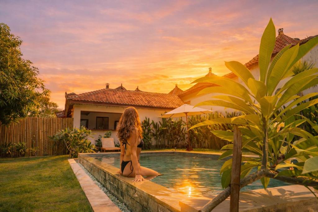 a woman is sitting next to a swimming pool at The Confidential Mandalika - Sea Front Hotel - New Starlink 70Mbps WiFi - Free Gym Access in Kuta Lombok