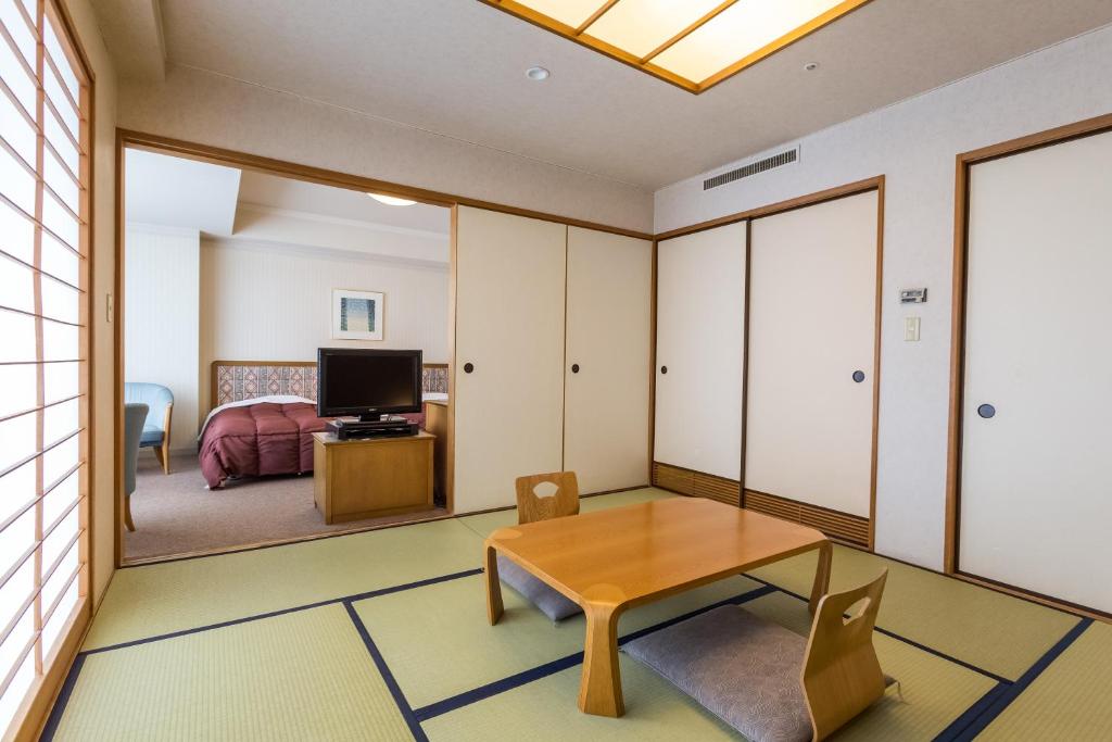 a living room with a table and a bedroom at Kusatsu Onsen Hotel Village in Kusatsu