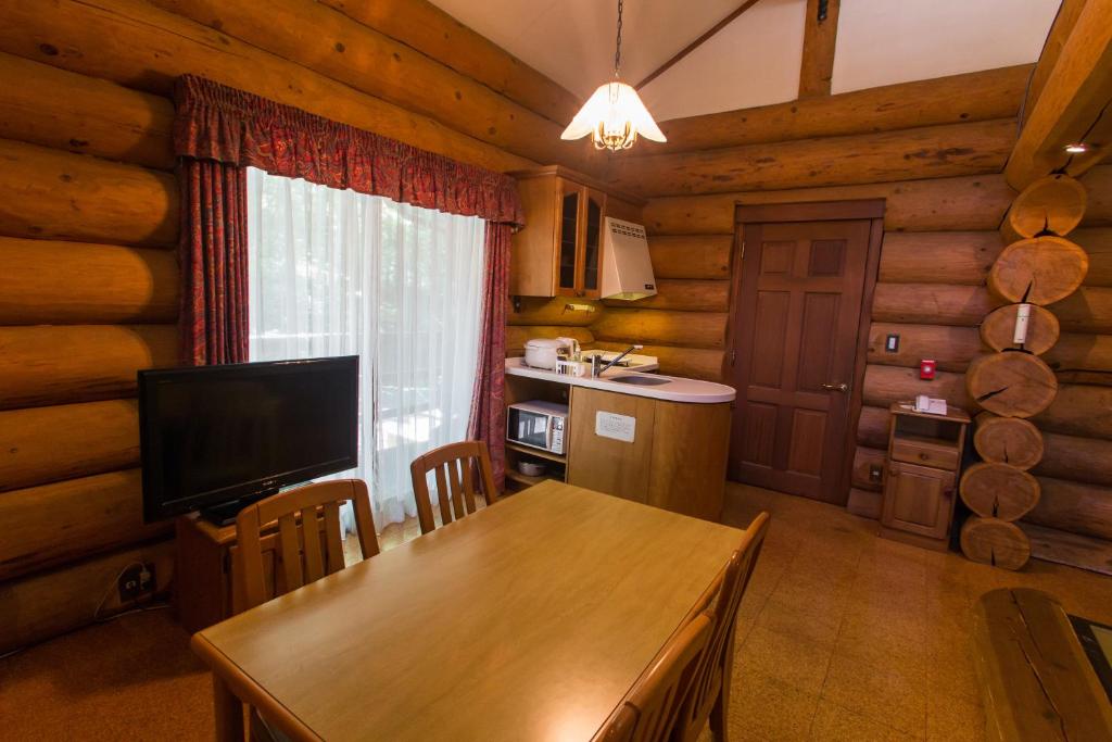 a kitchen and dining room with a table and a television at Kusatsu Onsen Hotel Village in Kusatsu