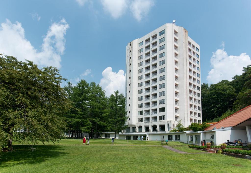 a large white building with a grass field in front at Kusatsu Onsen Hotel Village in Kusatsu