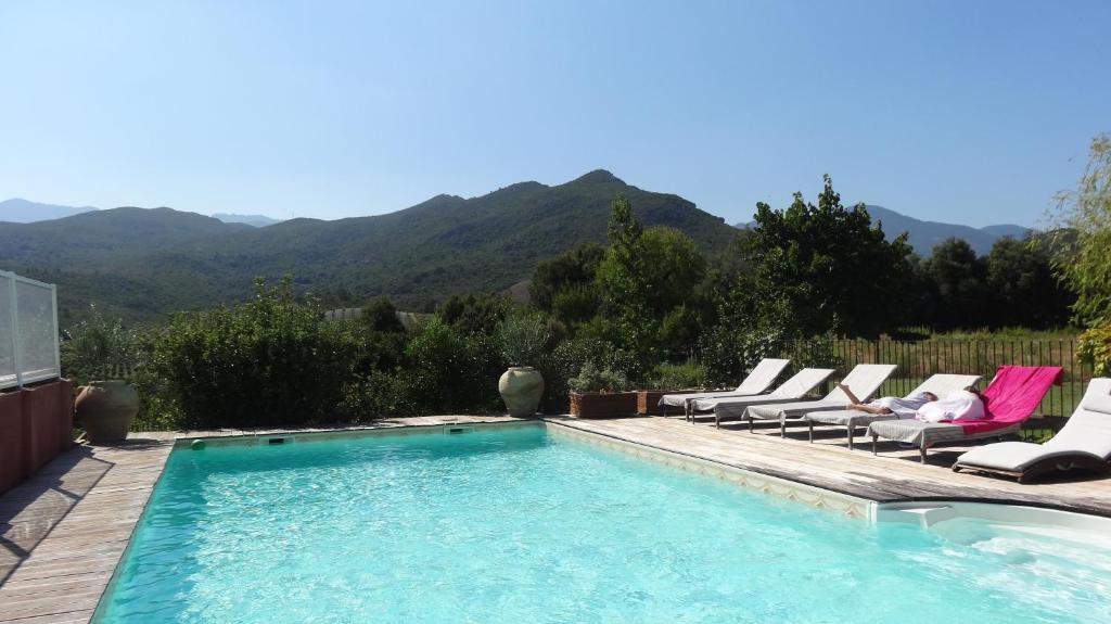 a swimming pool with lounge chairs and mountains in the background at E case di u Puntale in Ghisonaccia