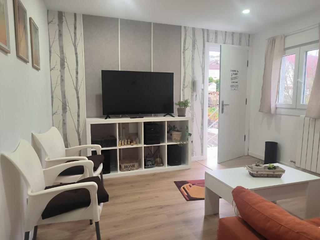 a living room with a flat screen tv and white chairs at Los Cala-Vivienda tranquila en casa unifamiliar in Vigo