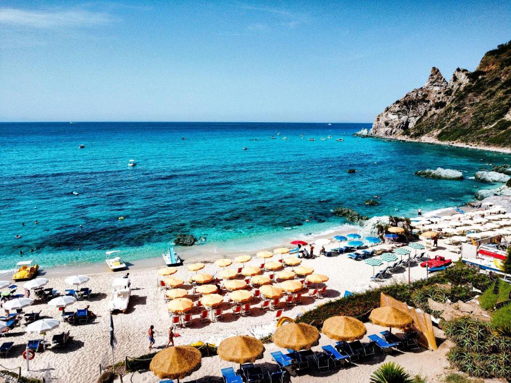 a beach with a bunch of umbrellas and the ocean at Costa Real - Garden Retreat with Private beach, Pet Friendly in Capo Vaticano