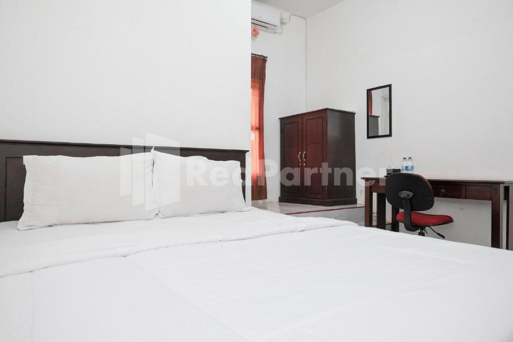 a bedroom with a large white bed and a desk at Katup Guest House Syariah Mitra RedDoorz in Yogyakarta