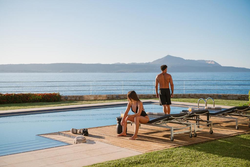 a man and a woman standing next to a swimming pool at SK Place Luxury Seafront Villas Chania in Almyrida