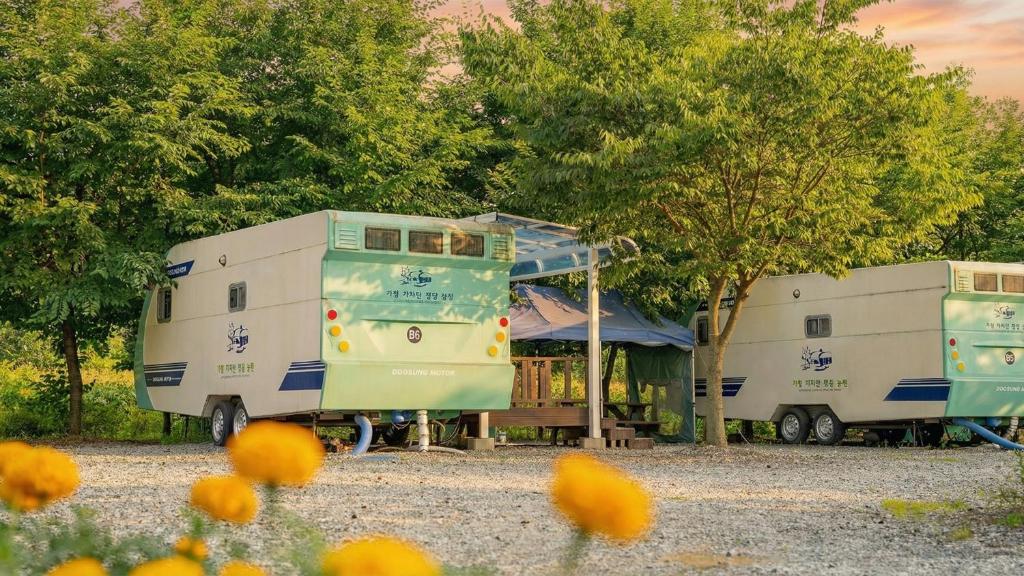 two rvs parked next to each other with trees at Gapyeong Karabankaempingnongwon in Gapyeong