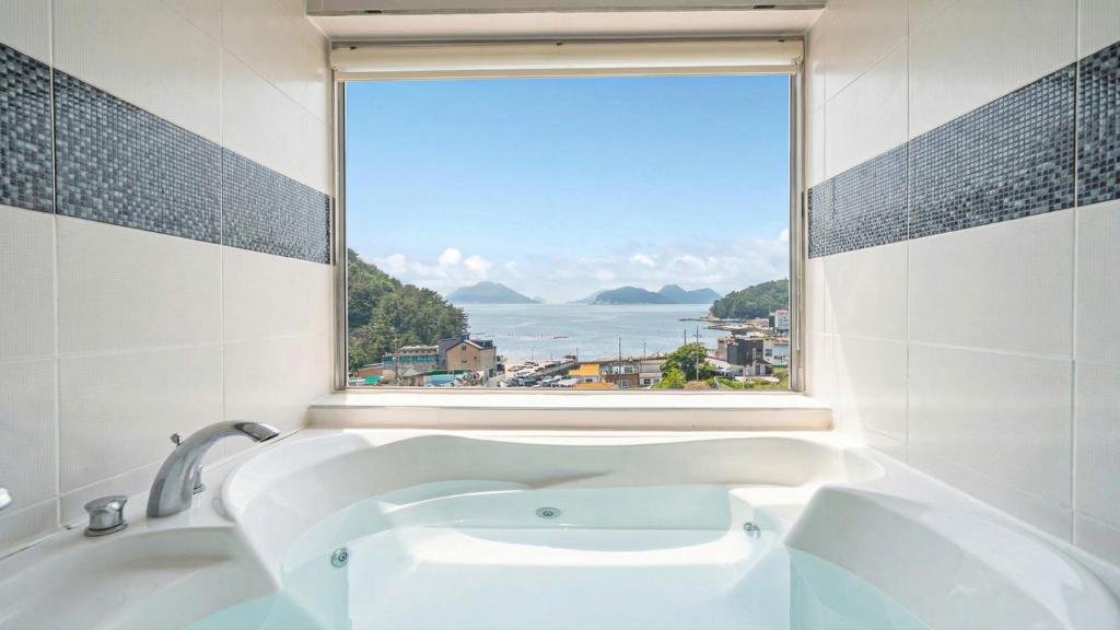 a bathroom with a bath tub with a window at Geoje Gaonara Pension in Geoje