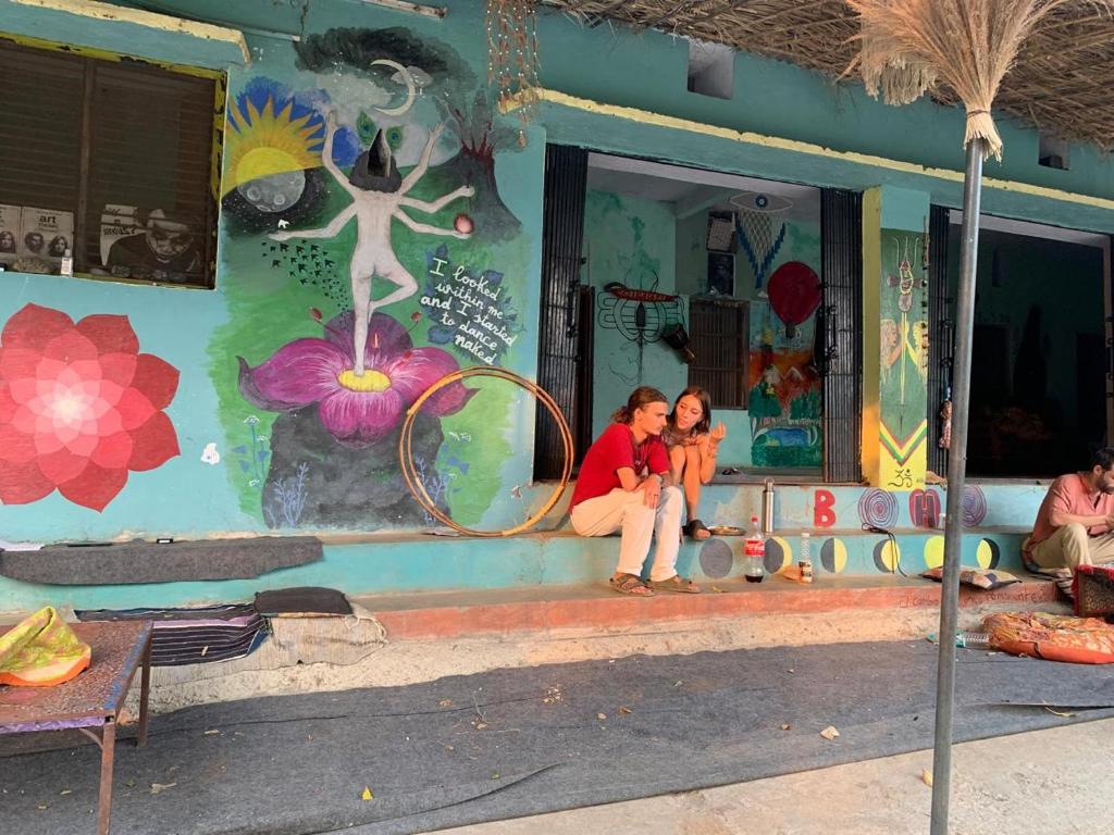 two people sitting on the porch of a building with a mural at Clan BoHo - WiFi enabled mountain stay with nourishing farm to table meals in Rishīkesh