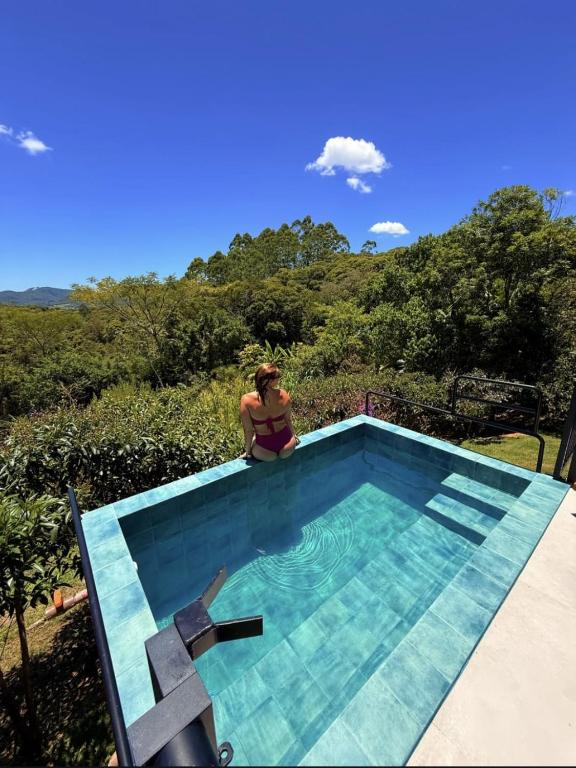 a woman sitting on the edge of a swimming pool at Recanto Vera Lucia in Santo Amaro da Imperatriz