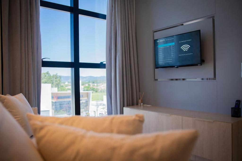a living room with a tv and a couch and a window at Studio Completo Perto Hospital e Shopping in Tubarão