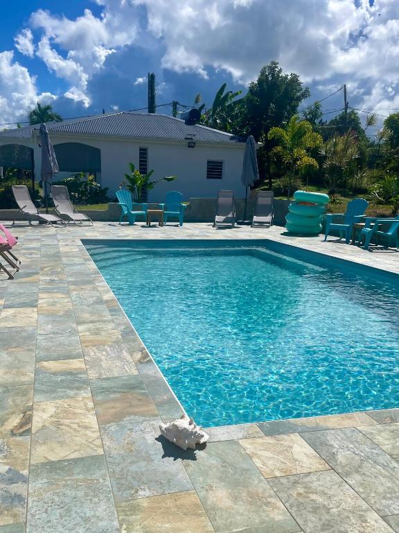 a swimming pool with blue chairs and a house at Coco-orchidées Le Domaine Mannou in Sainte-Rose