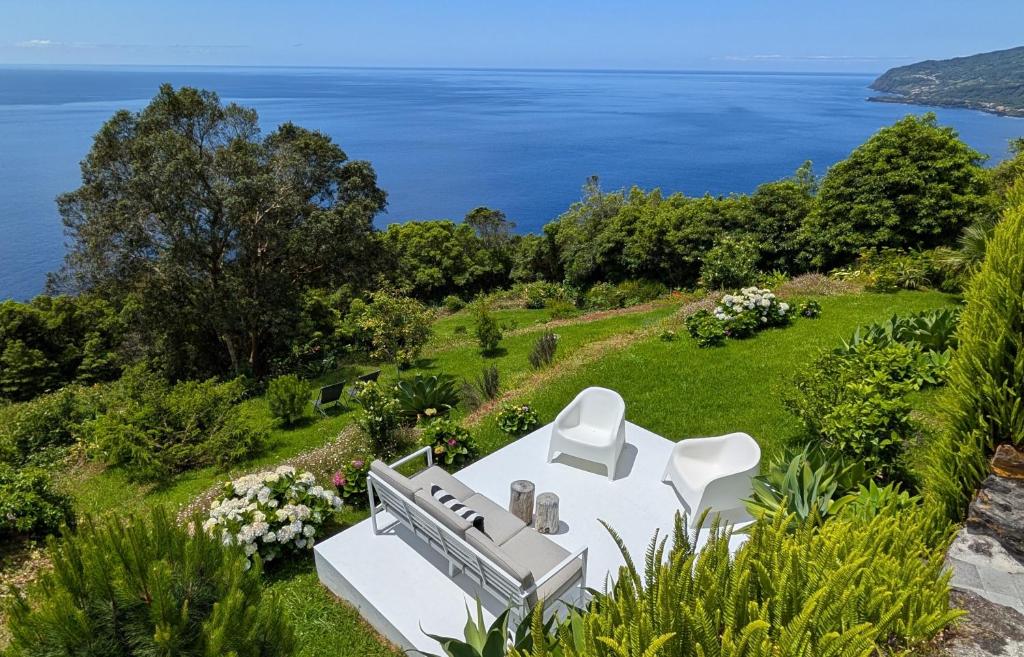 a white bench sitting on top of a field with the ocean at Casas do Horizonte in Ribeiras