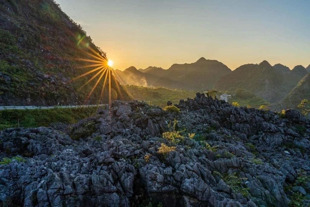 a sun setting over a rocky hill with mountains in the background at Easy Ha Giang in Làng Lap