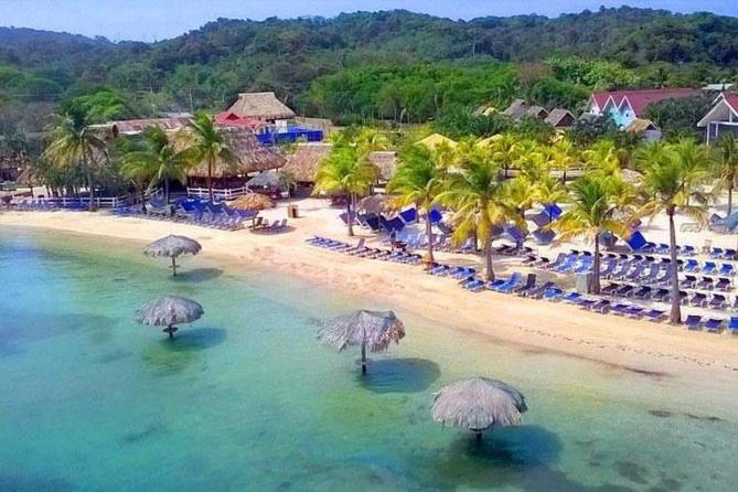 an aerial view of a beach with umbrellas in the water at Las Palmas Beach Roatan in Dixon Cove