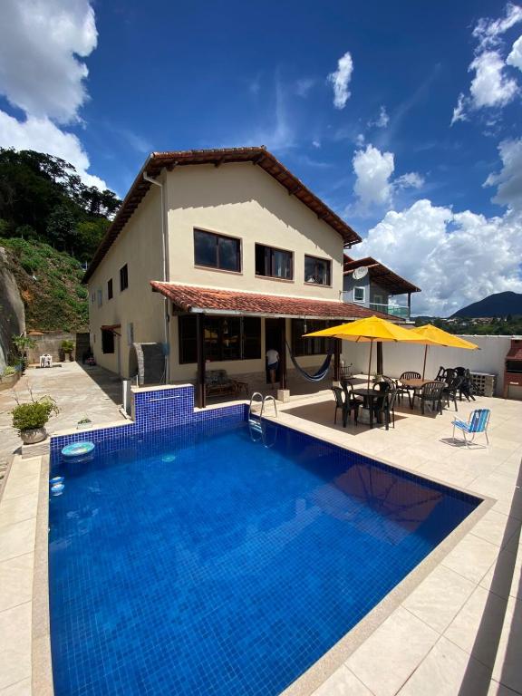 a villa with a swimming pool in front of a house at Pousada Por do Sol in Teresópolis