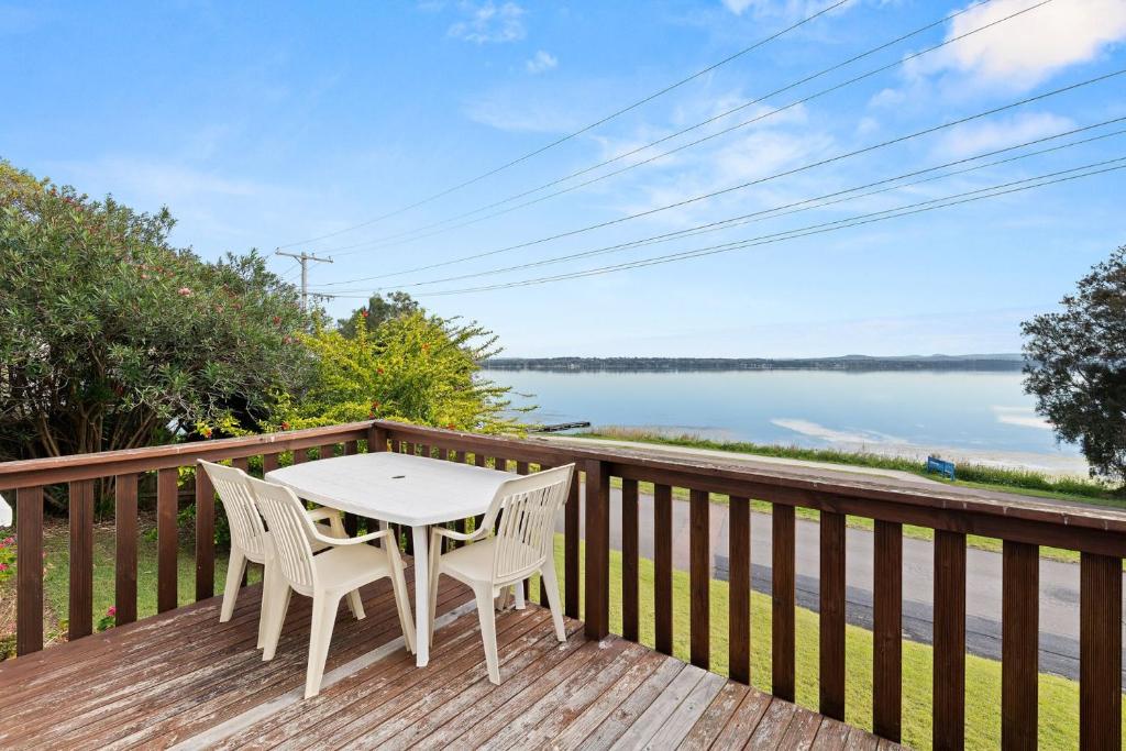 a table and chairs on a deck with a view of the water at Sunbeam Cottage on the Lake in Toukley