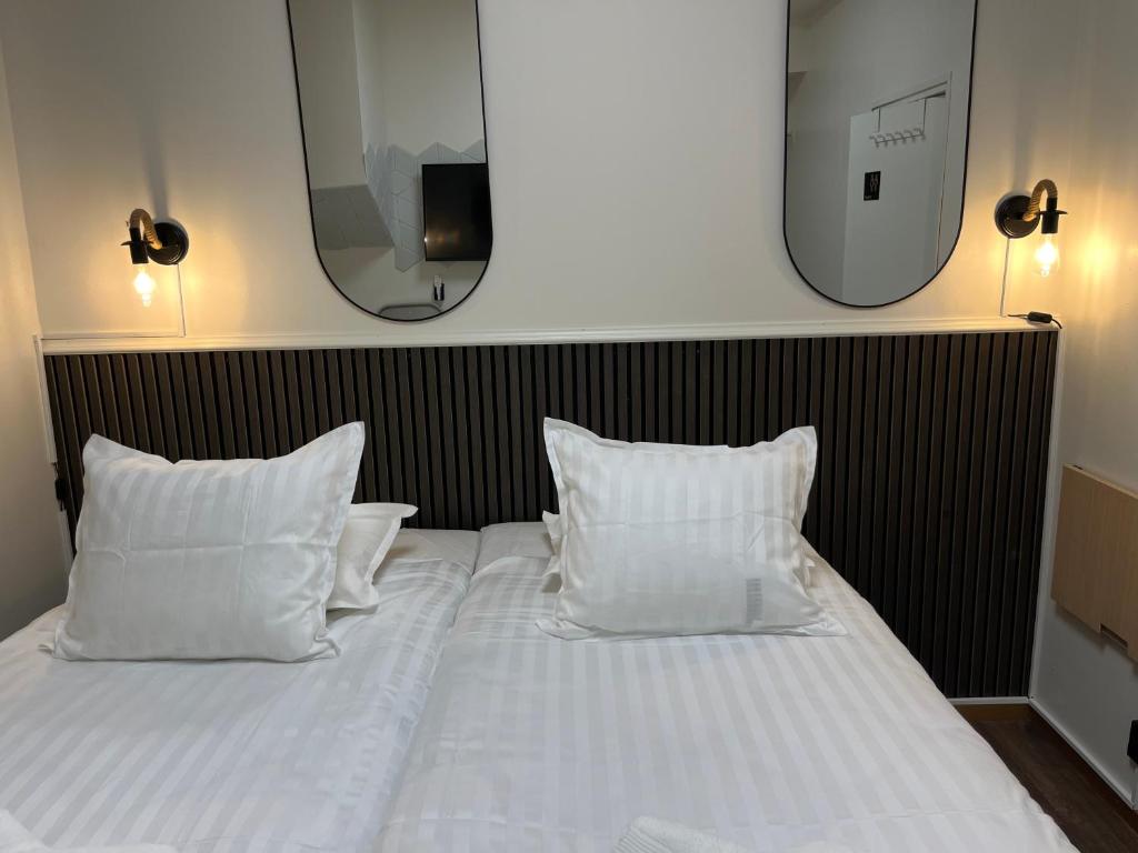 a bed with white pillows and a mirror on the wall at Oxbackens Hotell & Café in Västerås