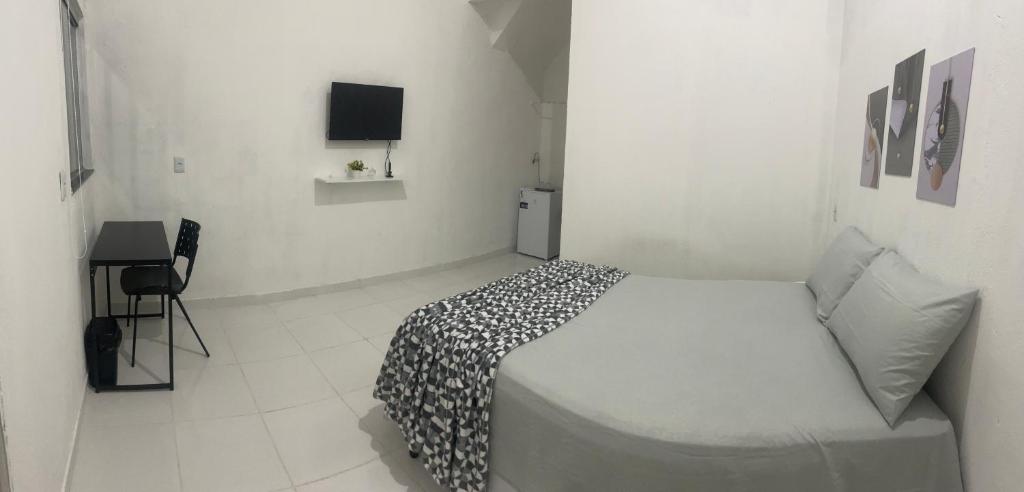 a white bedroom with a bed and a television at Suítes JK in Paragominas