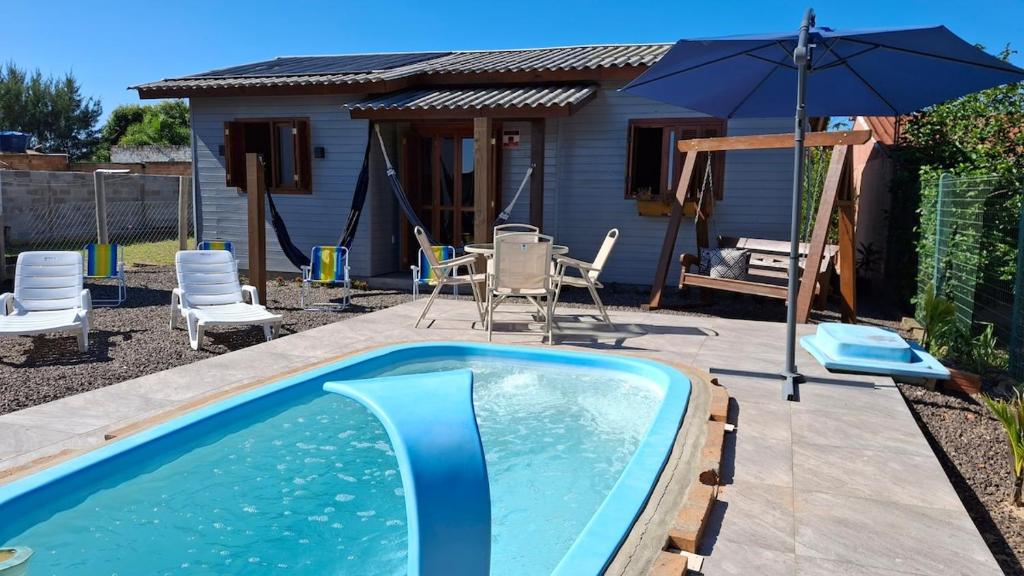 a swimming pool with an umbrella next to a house at Casa com piscina aquecida, 3 quartos e 3 camas extras in Capão da Canoa