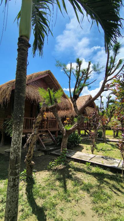 a hut with a palm tree in front of it at Garden Cottage in Gili Gede