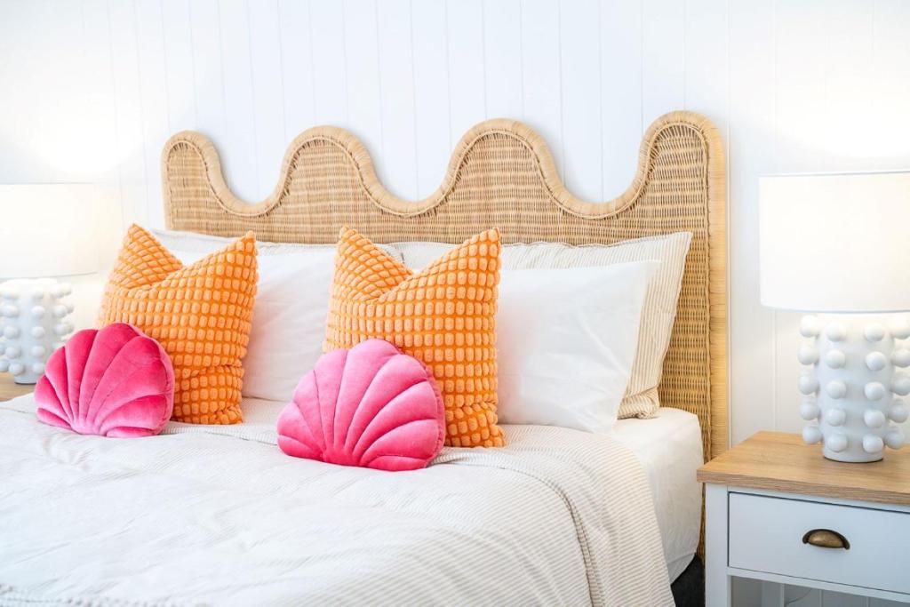 a bed with orange and pink pillows on it at The Chelsea Beachside Apartment in The Entrance
