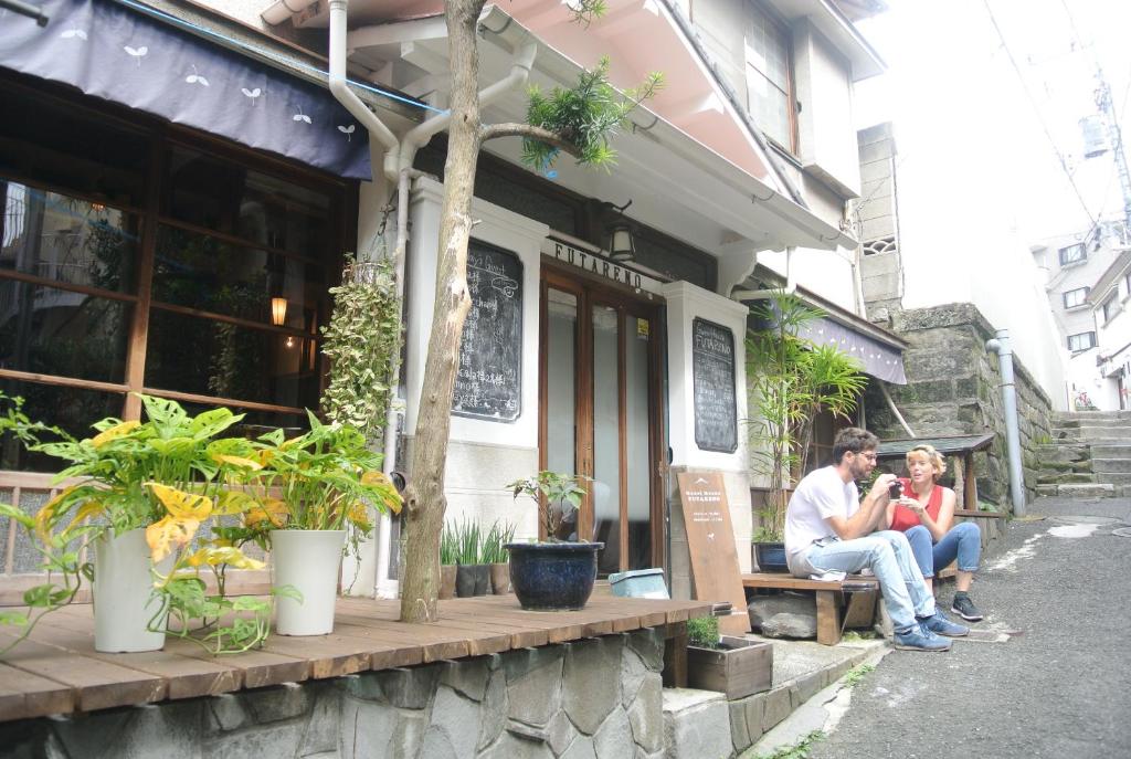 dos personas sentadas en un banco fuera de un edificio en Guest House FUTARENO, en Yokohama